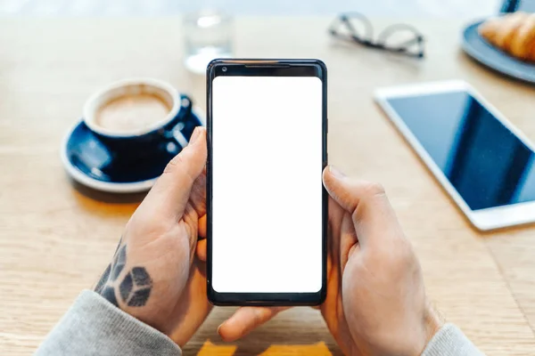 空白の画面を持つ携帯電話を保持している入れ墨男の手のクローズ アップ. — ストック写真