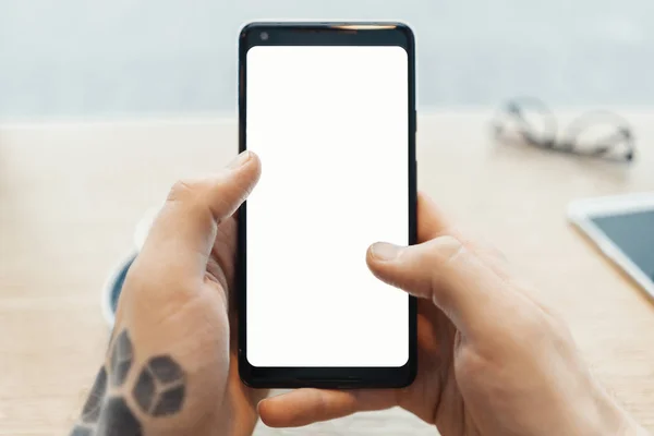 Primer plano del hombre tatuado manos sosteniendo el teléfono móvil con pantalla en blanco . — Foto de Stock