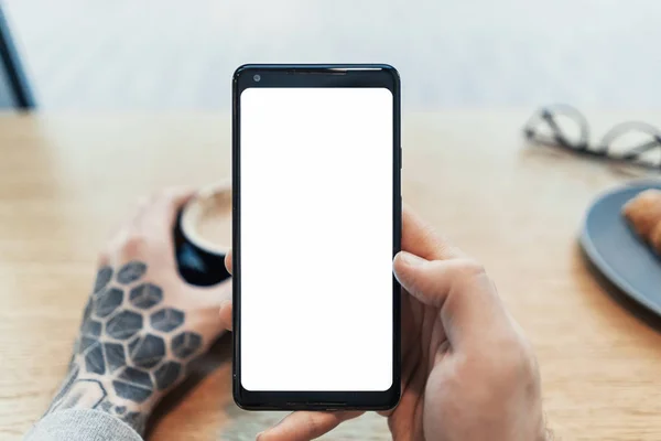 空白の画面を持つ携帯電話を保持している入れ墨男の手のクローズ アップ. — ストック写真