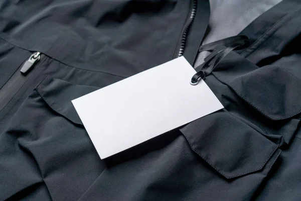 Prázdné bílé obdélníkové oblečení Tag, Label Mockup šablona na černé stylové sportovní oblečení. Cenový štítek s kopírovacím prostorem, prázdné místo — Stock fotografie