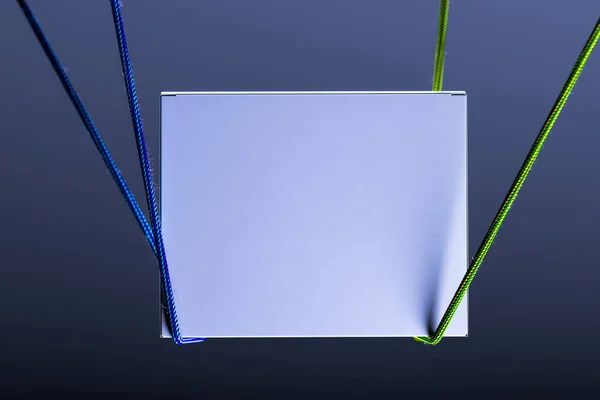 Modelo de sinalização quadrangular branco em branco no fundo escuro iluminado pela luz e amarrado com cordas. Renderização 3d — Fotografia de Stock