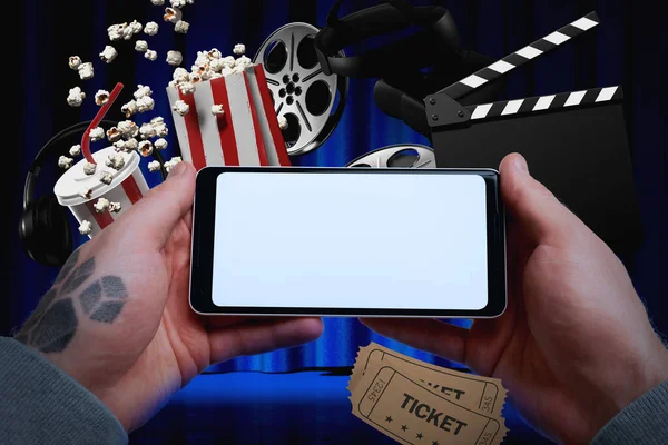 2017 년 1 월 20 일에 확인 함 . Tattooed Man Hands Holding Modern Mobile Phone With White Blank Screen on Clapper, Popcorn, Reel Background. 온라인 영화의 개념. 3d 렌더링 — 스톡 사진