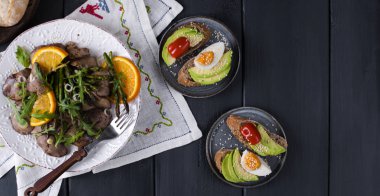 Tai yemekleri, roka ile bir tabak kızarmış tavuk karaciğer ve turuncu. Siyah ahşap arka plan üzerinde. Ekmek, ekmek avokado ve suyu. Sağlıklı öğle yemeği. Kopya alanı