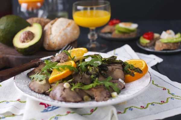 Um delicioso jantar saudável, uma salada de fígado de frango quente com laranjas e rúcula, em um fundo de madeira preta. Sumo de laranja e pão fresco com abacate. Espaço livre para texto. Espaço de cópia . — Fotografia de Stock