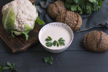 Kremalı karnabahar çorbası ile krem ve Yeşiller, bir ahşap tahta ve siyah arka plan üzerinde beyaz bir fincan. Vintage Fotoğraf. Taze yeşillik, karnabahar ve tahıl ekmek. Sağlıklı fitness yemek. Kopya alanı