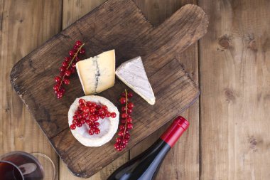 Peynir ve kırmızı şarap. Beyaz ve mavi kalıp farklı peynir. Çilek kırmızı kuş üzümü, beyaz çiçekler. Ahşap arka plan ve metin veya reklam için boş alan. sapce kopyalayın. düz lay