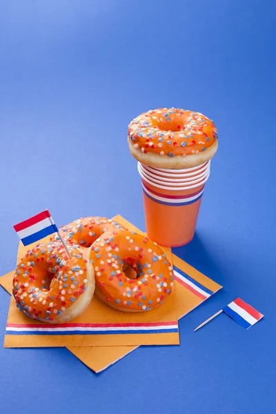 Viering van de dag van de koningen in Nederland. Leuke vakantie. Oranje zoete donuts en glazen op een blauwe achtergrond en vlaggen. Vrije ruimte voor tekst. Sivol vakantie — Stockfoto