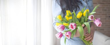Bir kadın bir buket taze lale tutuyor. Çiçekler sarı ve pembe. Pencerenin yanındaki kız. Metin için yer.