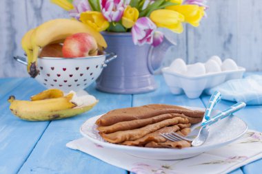 bir buket sarı ve pembe ve çiçek ve krep taze lale. Mavi arka plan. Bahar. Bir vazo içinde meyve.