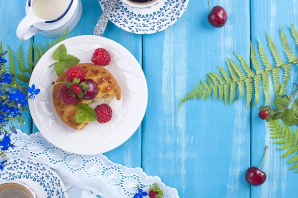 Çilek, çilek ve vişne ile küçük cupcakes. Lezzetli tatlı kahvaltı ve hoş kokulu kahve, mavi ahşap arka plan ve çiçekler. Uzay kopyalayın. Yukarıda. düz lay.