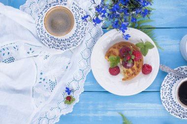 Çilek, çilek ve vişne ile küçük cupcakes. Lezzetli tatlı kahvaltı ve hoş kokulu kahve, mavi ahşap arka plan ve çiçekler. Uzay kopyalayın. Yukarıda. düz lay