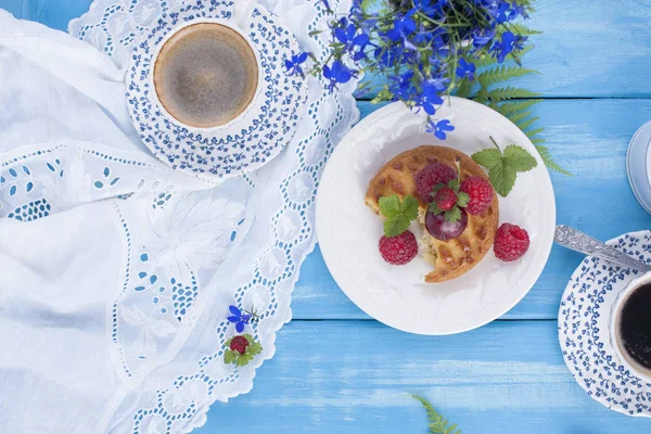 Çilek, çilek ve vişne ile küçük cupcakes. Lezzetli tatlı kahvaltı ve hoş kokulu kahve, mavi ahşap arka plan ve çiçekler. Uzay kopyalayın. Yukarıda. düz lay