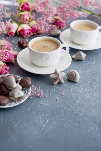 Eine Tasse duftenden Kaffee am Morgen und einen Strauß rosa Blumen. Schokoladenbonbons in Form von Herzmuscheln. Muscheln auf den Tassen. Romantik und helle Farben. Guten Morgen. Postkarte. Platz für tex — Stockfoto