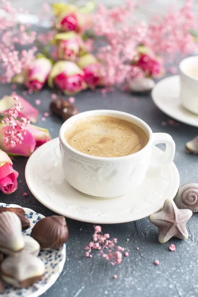 Eine Tasse duftenden Kaffee am Morgen und einen Strauß rosa Blumen. Schokoladenbonbons in Form von Herzmuscheln. Muscheln auf den Tassen. Romantik und helle Farben — Stockfoto