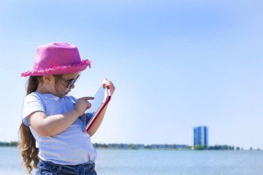 Elinde bir tablet bilgisayar ile küçük kız. Plaj ve mavi gökyüzü güneşli günde. Kopya alanı