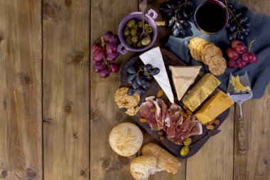 Şarap için snack. Jambon, farklı peynir, zeytin, üzüm, ekmek ve bir bardak kırmızı şarap. Ahşap arka plan. İtalyan yemeği. kopya alanı. düz lay