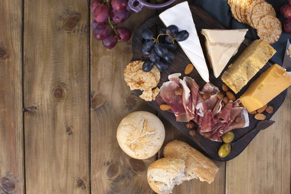 Şarap için snack. Jambon, farklı peynir, zeytin, üzüm, ekmek ve bir bardak kırmızı şarap. Ahşap arka plan. İtalyan yemeği. kopya alanı. düz lay