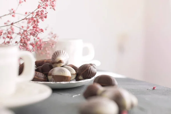 Dulces de chocolate en forma de conchas y dos tazas de café fragante. Desayuno romántico. Colores claros. Flores rosas. Espacio libre para texto. espacio de copia — Foto de Stock