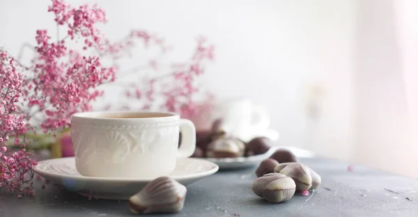 Dulces de chocolate en forma de conchas y dos tazas de café fragante. Desayuno romántico. Colores claros. Flores rosas. Espacio libre para texto. espacio de copia — Foto de Stock