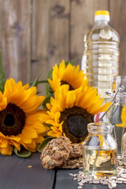 Ayçiçek yağı ve büyük sarı çiçekler. Petrol şişe. Ahşap arka plan, tohumlar ve fındık ve tohum ile bisküvi. Organik gıda. Kopya alanı