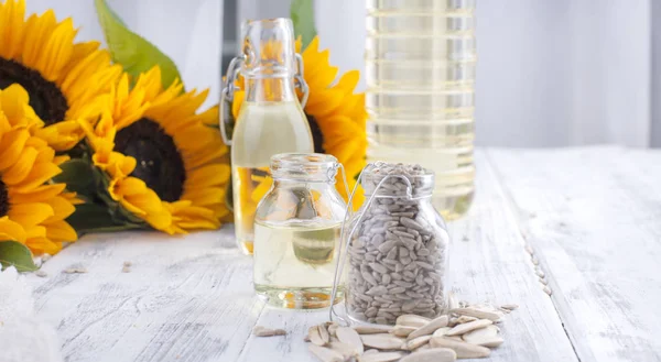 Ayçiçek yağı ve büyük sarı çiçekler. Petrol şişe. Ayçekirdeği kabuğu. Beyaz ahşap arka plan. Vintage Fotoğraf. Organik gıda. Kopya alanı.