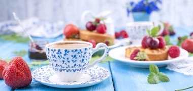 Lezzetli yaz kahvaltı, ev yapımı hamur işleri ve hoş kokulu kahve. Mavi ahşap arka plan, çilek ve yeşil yaprakları ve çiçekleri üzerinde. Uzay kopyalayın. Afiş