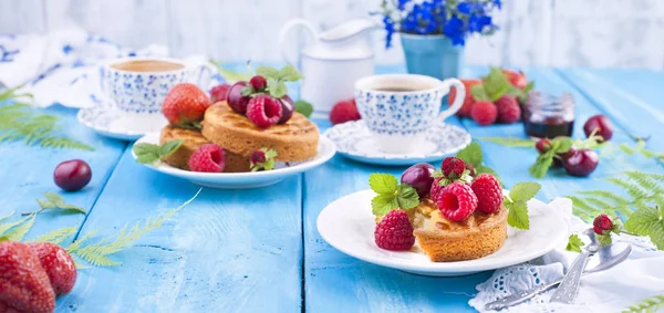 Lezzetli yaz kahvaltı, ev yapımı hamur işleri ve hoş kokulu kahve. Mavi ahşap arka plan, çilek ve yeşil yaprakları ve çiçekleri üzerinde. Kopya alanı