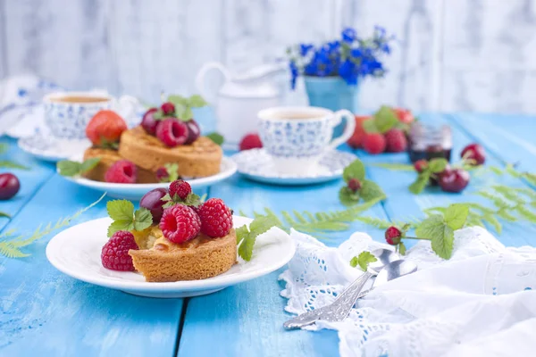 Lezzetli yaz kahvaltı, ev yapımı hamur işleri ve hoş kokulu kahve. Mavi ahşap arka plan, çilek ve yeşil yaprakları ve çiçekleri üzerinde. Kopya alanı.