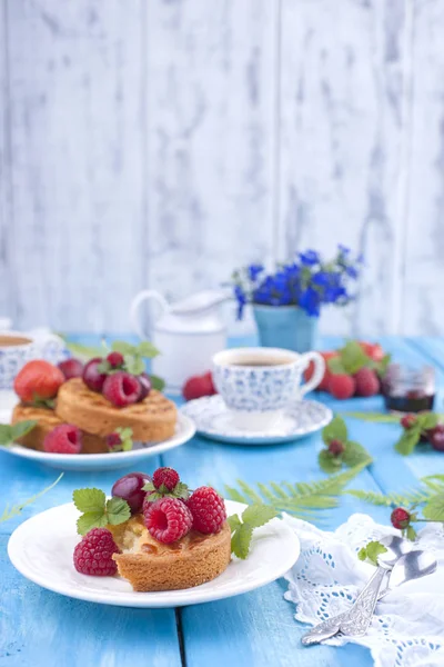 Lezzetli yaz kahvaltı, ev yapımı hamur işleri ve hoş kokulu kahve. Mavi ahşap arka plan, çilek ve yeşil yaprakları ve çiçekleri üzerinde. Kopya alanı