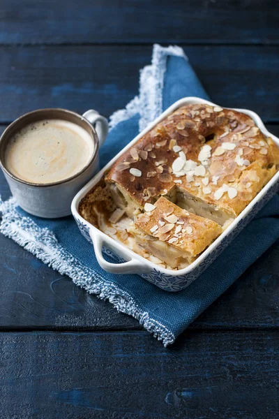 Sweet home-made pie with almonds for breakfast, fragrant coffee with foam, on a blue towel and a black background.