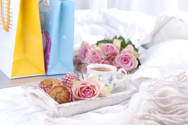a white bed, packages with gifts, fresh coffee, breakfast cakes and a bouquet of pink roses. Good morning Vintage photo. copy space