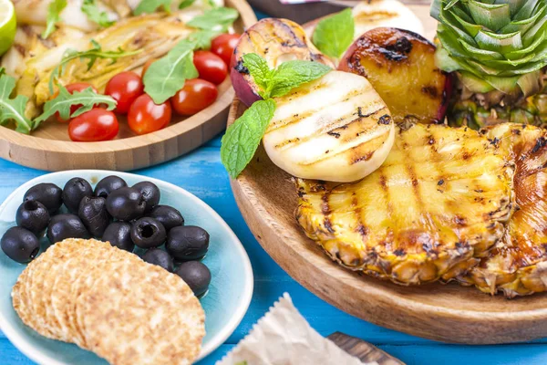 Grilled vegetables, shrimp, fruit on a wooden plate and sausages, juice and salad on a blue background. Summer dinner. Free space for text. Copy space