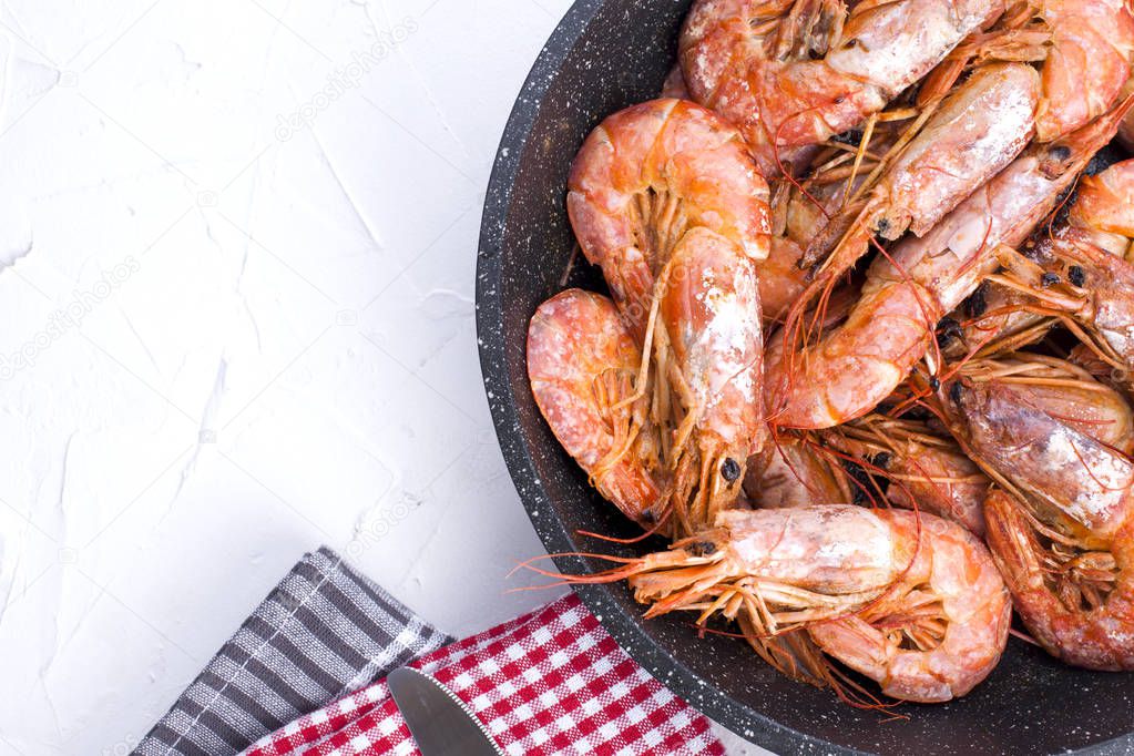 Large shrimps fried in a frying pan. On a white table. Lunch from seafood. Free space for text. Copy space