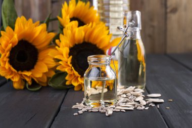 Dodsolnechnoe yağda bir büyük ve küçük bir şişe, bir buket ayçiçeği, küçük bir arka plan ve dağınık tohumları. Doğal ürün, rustik tarzı. Kopya alanı.