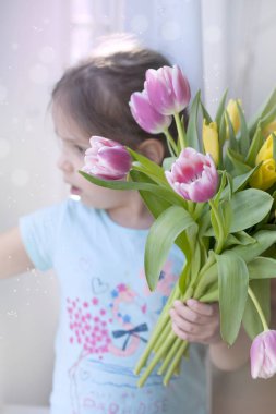 bahar çiçekleri Not kızla. Pencerenin yanındaki oturma odasında rahat bir evde. Farklı renklerde laleler. Bir kadının günde bir hediye.