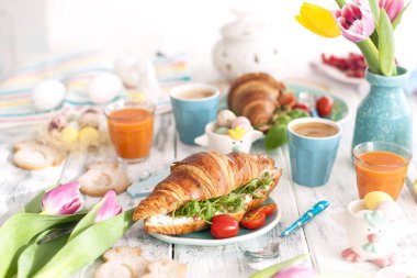 Farklı renkler ile arka plan. Kruvasan roket ve peynir ve aromatik kahveler, farklı renkler, parlak yemekleri ve Paskalya dekor, seramik tavşan yumurta ile bir aile kahvaltı