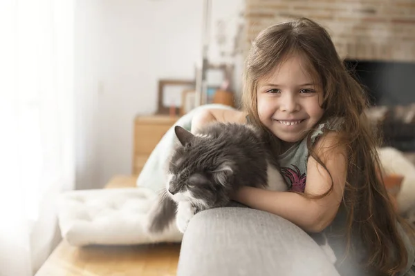 Menina e gato em casa no sofá. Uma criança feliz e um animal de estimação. Espaço de cópia — Fotografia de Stock