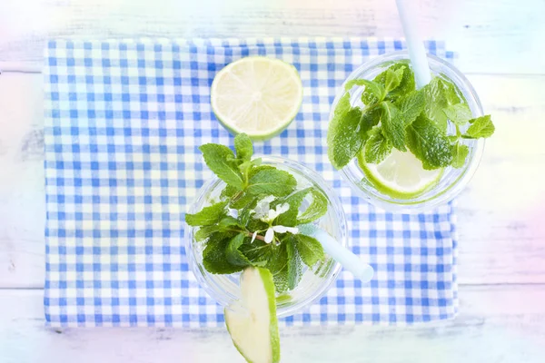 İki bardak su ve taze yeşil nane ve limon. Bir ahşap zemin üzerinde mavi bir peçeteye. Kartpostal.