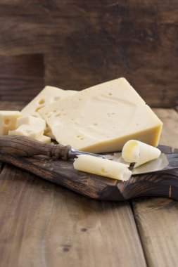 Peynir delikli ahşap masa üzerinde yararlı bir süt ürün parçaları olarak kesilir. Lezzetli yemekler. Ülke tarzı fotoğraf. Metin için yer. Kopya alanı