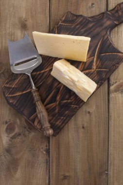 Peynir delikli ahşap masa üzerinde yararlı bir süt ürün parçaları olarak kesilir. Lezzetli yemekler. Ülke tarzı fotoğraf. Metin için yer. Kopya alanı