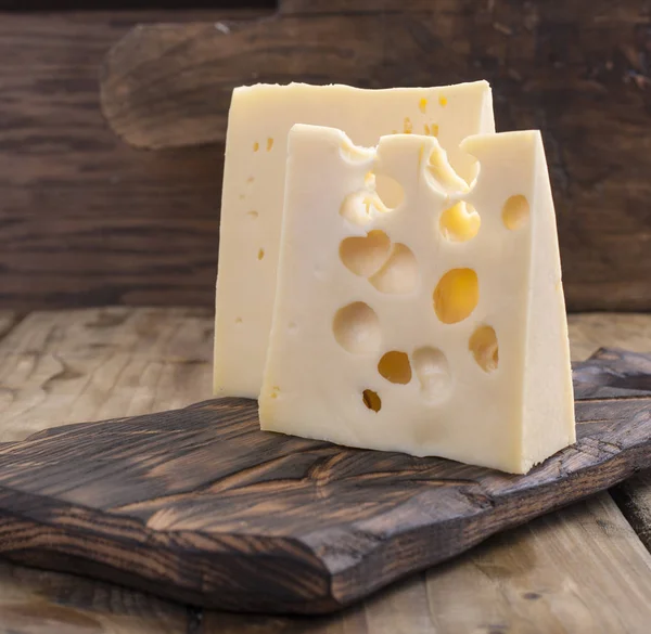 Peynir delikli ahşap masa üzerinde yararlı bir süt ürün parçaları olarak kesilir. Lezzetli yemekler. Ülke tarzı fotoğraf. Metin için yer. Kopya alanı — Stok fotoğraf
