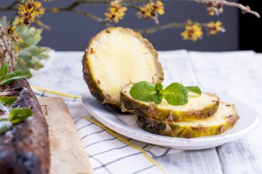 Ananas dilimleri ve nane kesilir. Beyaz ahşap zemin.