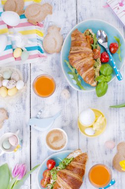 İki kişilik kahvaltı. Salata ve espresso ile ay çöreği. Taze meyve suyu ve tatlılar. Bahar lale. Paskalya dekor. Beyaz ahşap zemin.