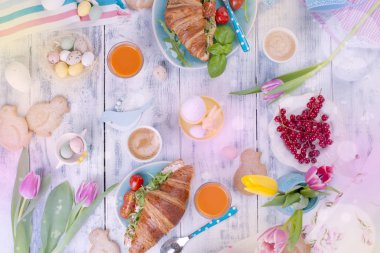 Farklı renkler ile arka plan. Kruvasan roket ve peynir ve aromatik kahveler, farklı renkler, parlak yemekleri ve Paskalya dekor, seramik tavşan yumurta ile bir aile kahvaltı. Taze laleler