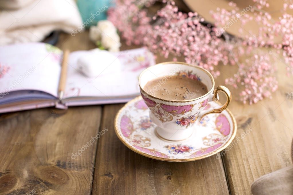 Aramatic coffee in a vintage bowl with a pattern. Planning the day in notepad. Decor of pink flowers. Cozy house. Free space for text. Card.