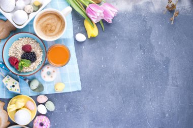 Arka plan gri taş üzerinde lezzetli bahar kahvaltı. Taze lale buketi. Küçük ve büyük renkli Paskalya yumurtaları. Yulaf ezmesi, kahve, taze çilek. Kartpostal Paskalya için.