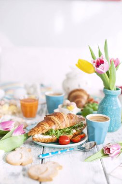 Paskalya kahvaltı. Kruvasan roket salata, peynir ve aromatik kahve ile bir aile kahvaltı. Taze lale pembe renkli ve farklı renklerde yumurta. Metin için özgür yer. Bahar için dekorasyon