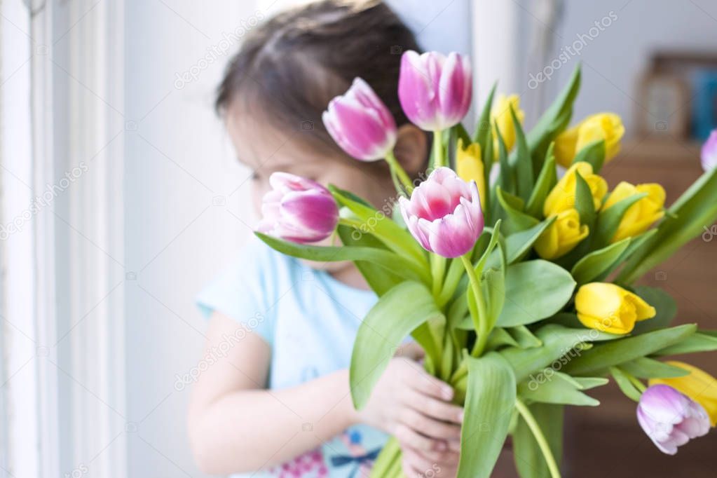 girl with a note of spring flowers. AT a cozy house in the living room by the window. Tulips of different colors. A gift on a womans day. Card. Free space for text or a postcard.