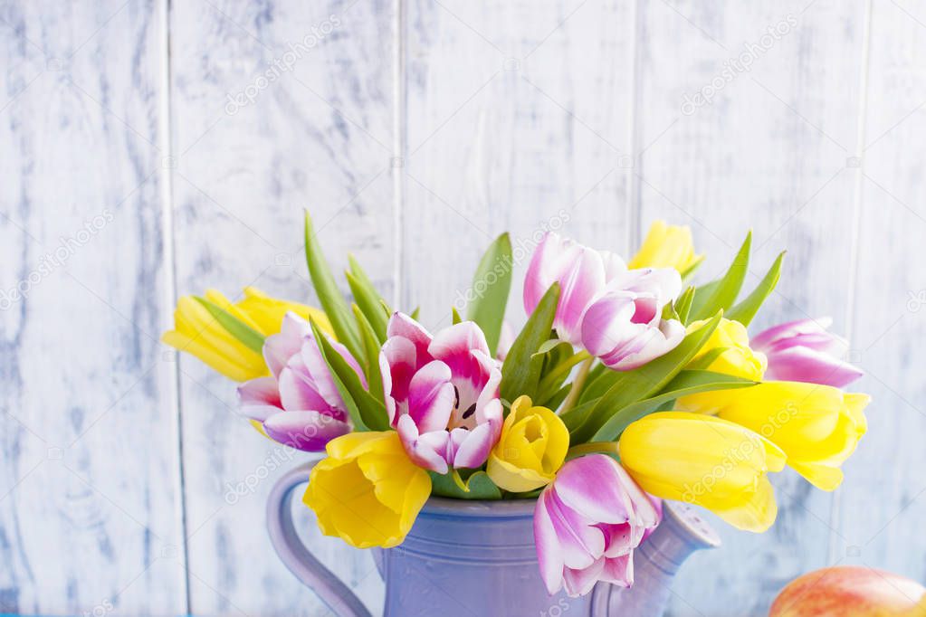 Spring tulips are pink and yellow. Different colors of eggs and pottery rabbit. Decor for Easter
