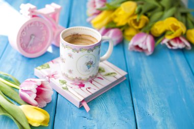 Bahar sabah, hoş kokulu kahve ve lale sarı ve pembe renk. Donuttsy kopyalar. Ahşap arka plan mavi, pembe çalar saat ve Not defteri, metin ve posta kartı için bir yer